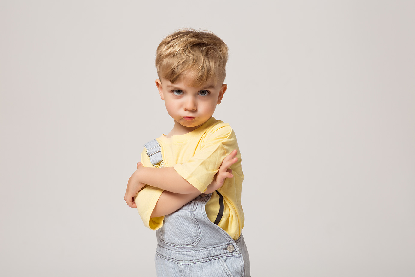 retrato de niño sobre fondo blanco con carita de enfadado y cruzando los brazos
