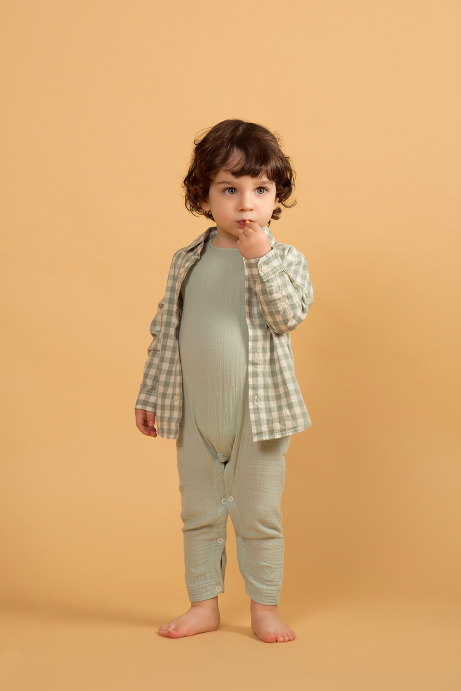 niño sobre fondo mostaza vestido de verde pastel comiendose una rosquilleta