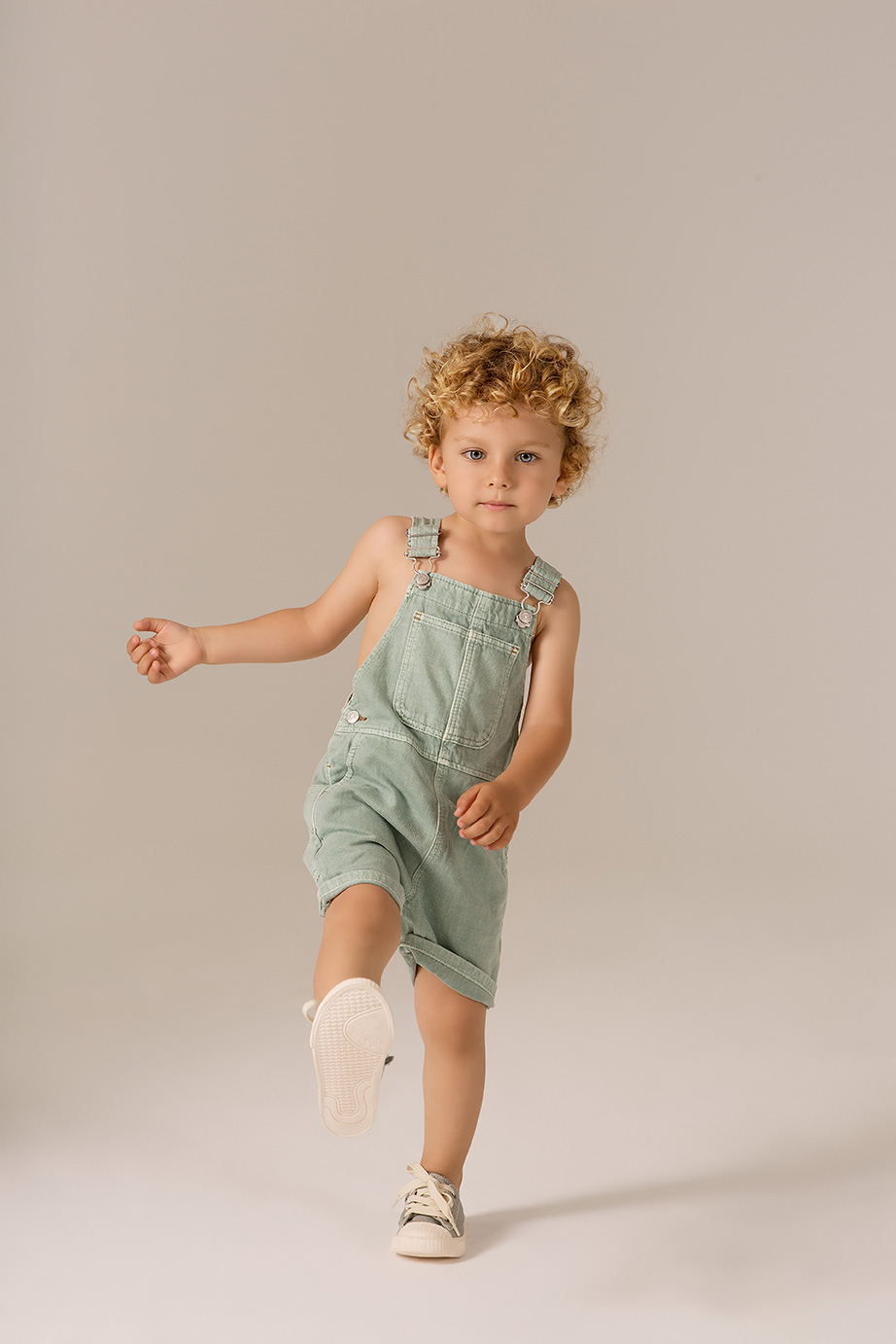 niño pequeño levantando la pierna con un mono vaquero verdoso