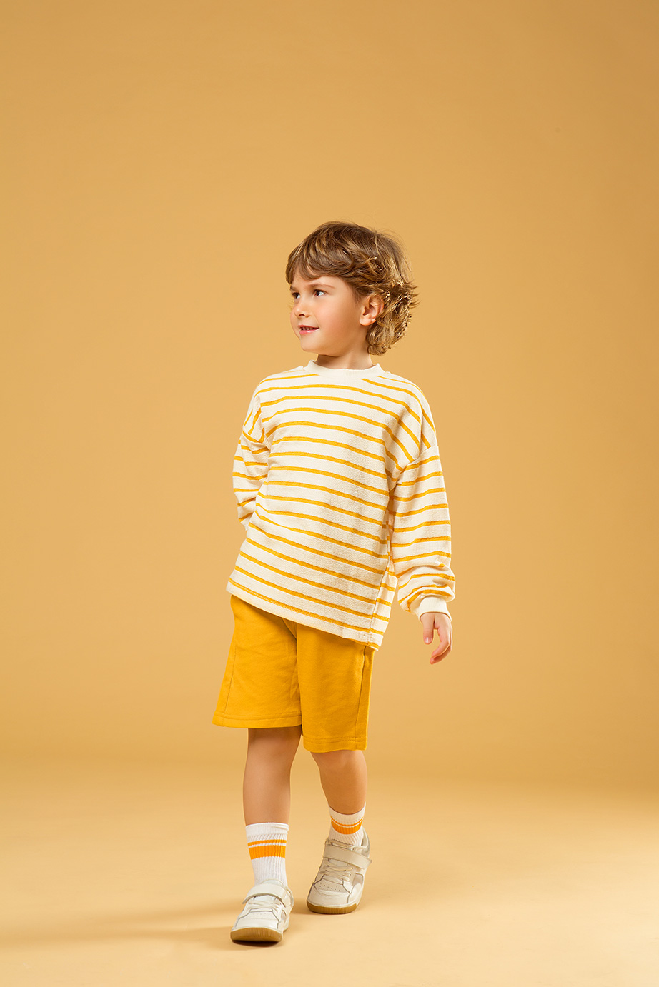foto de modelo de niño en fondo amarillo con sueter a rayas amarillas y pantalon amarillo