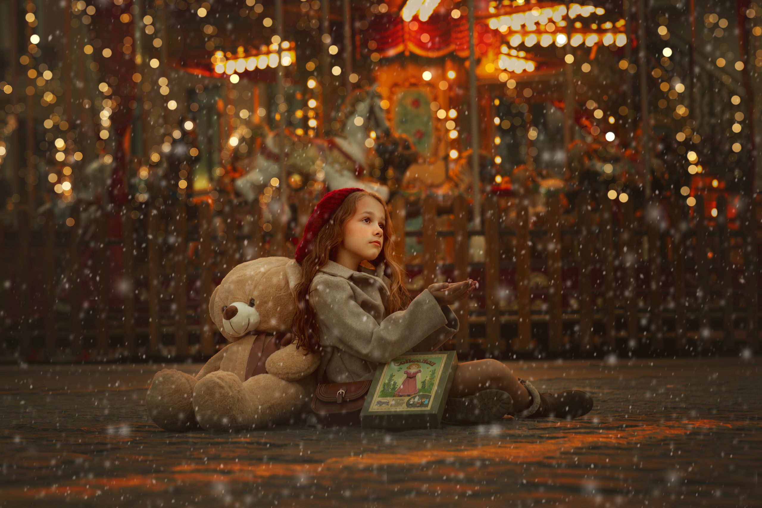 niña sentada con las manos como cogiendo nieve con un peluche de oso y un juego de muñecas antiguo vestida con abrigo gris y gorro de pompon rojo en el escenario el tiovivo de la estacion del norte de valencia en la foto hay luces navideñas y nieve cayendo