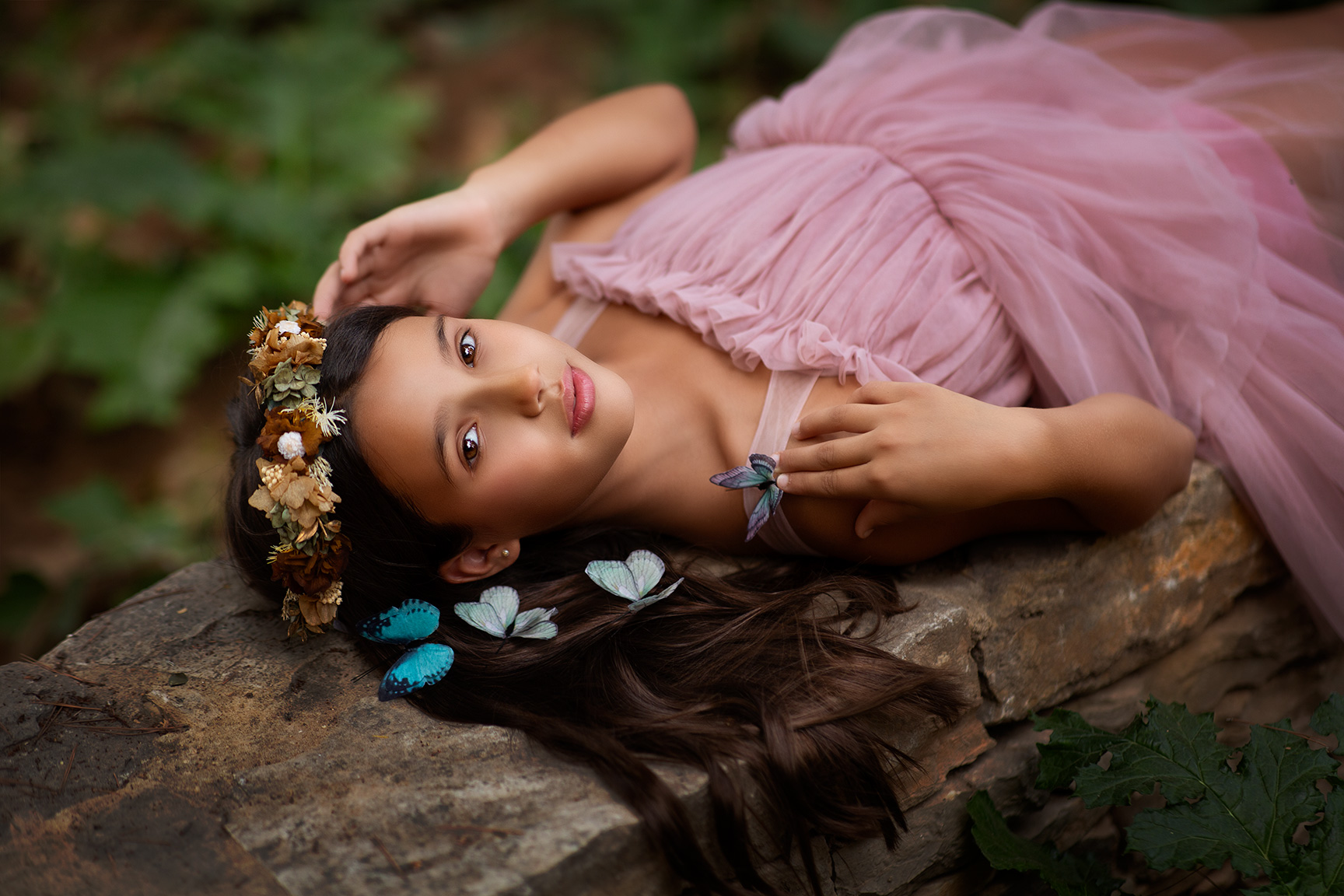 niña con traje rosa corona de flores y mariposas azules en el pelo posando para una sesion de fotos en la naturaleza en valencia
