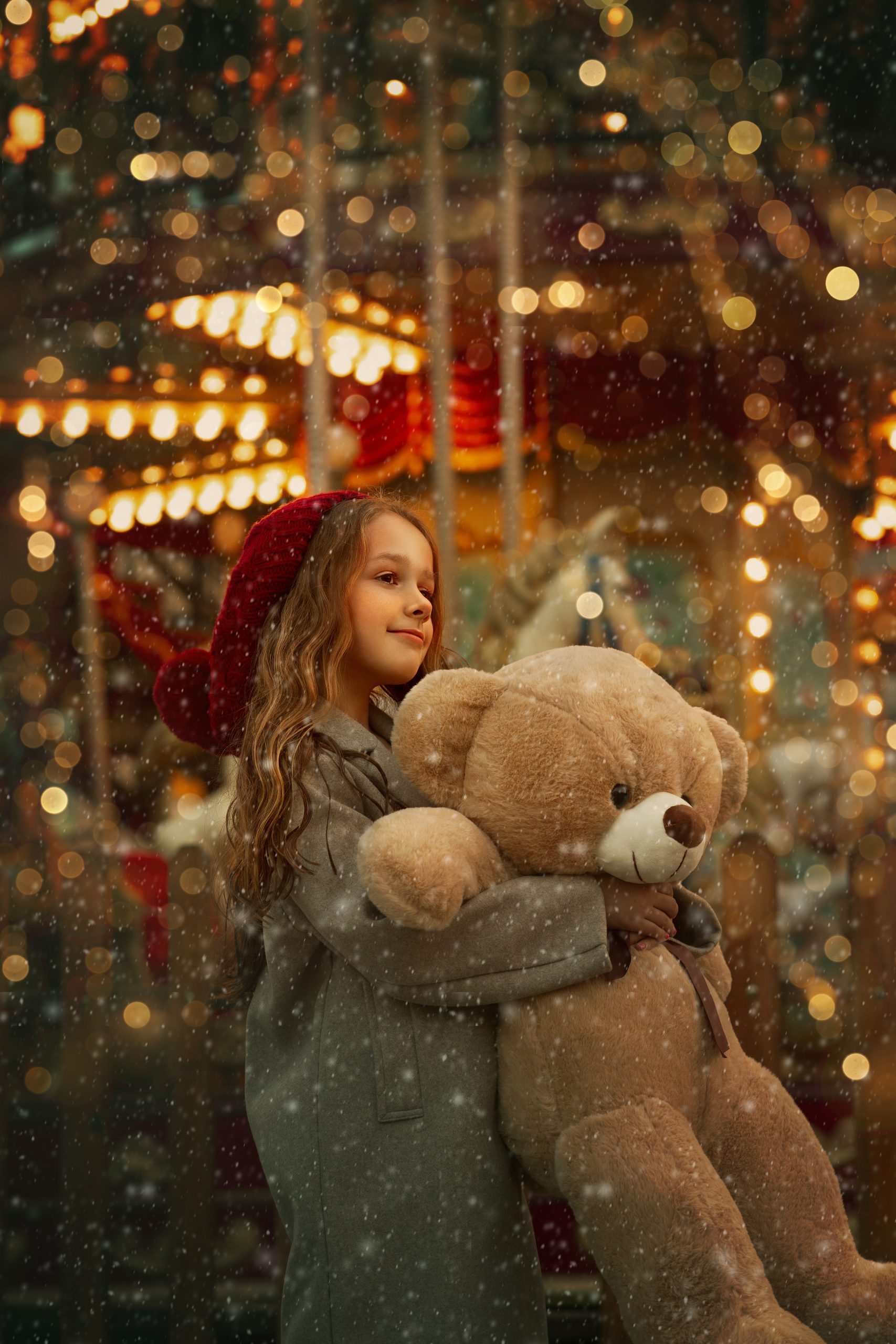 sesion-de-fotos-navidad-en-valencia-para-niños niña frente al tiovivo de valencia en una foto de navidad con nieve y luces abrazando un oso gigante de peluche