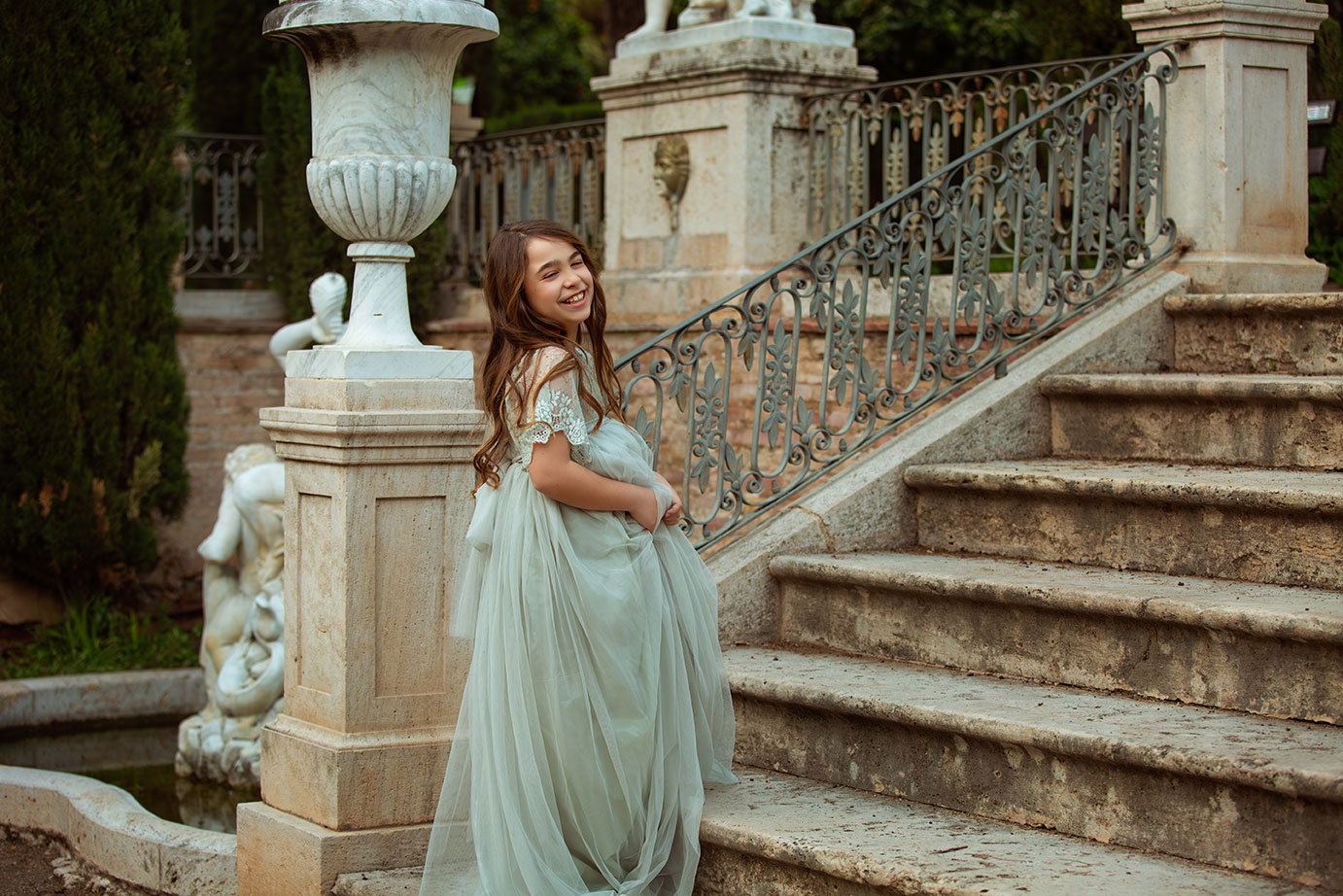 niña en su sesion de comunion en Valencia vestida con un traje verde de tul, subiendo unas escaleras en el jardín de monforte