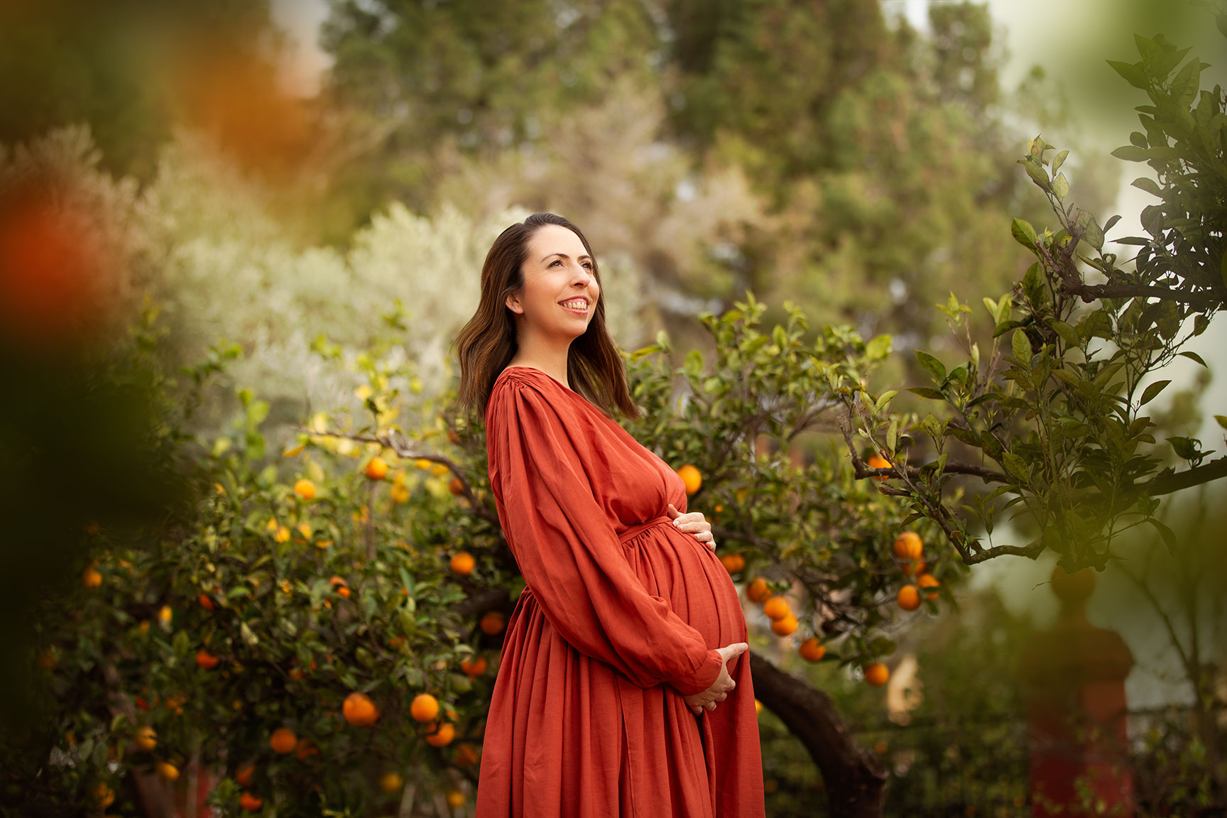 mujer embarazada en su sesion de embarazo en plena naturaleza vestida de naranja y tocandose la barriga