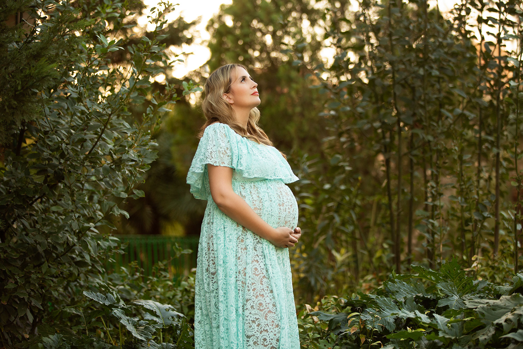 mujer embarazada en su sesion de embarazo en plena naturaleza vestida de azul y tocandose la barriga