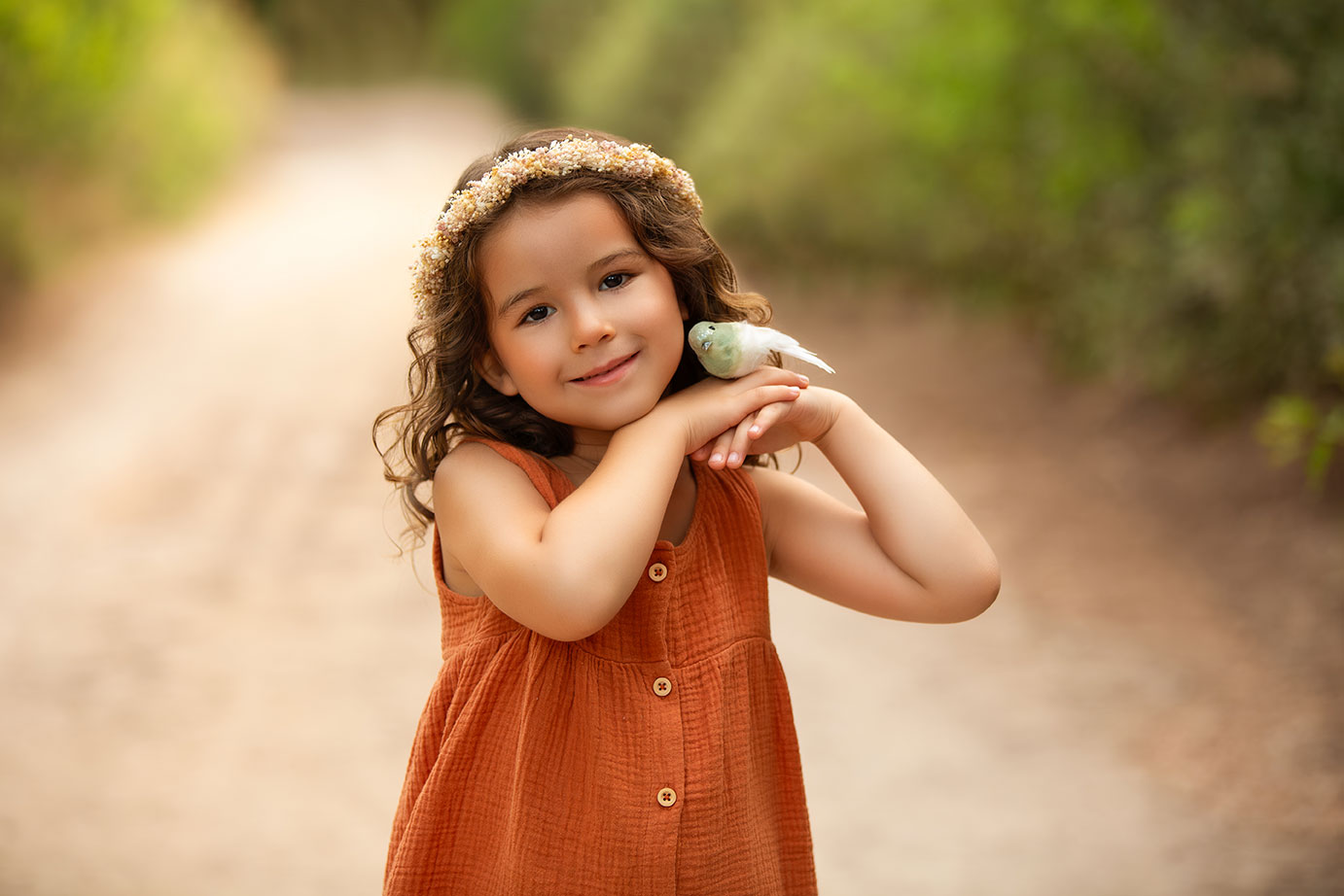 niña con vestida de color teja y corona de flores y sosteniendo un pajarito artificial , en su sesion infantil y familiar en la naturaleza en valencia